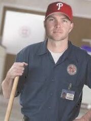 Janitor with broom handle, red baseball cap.